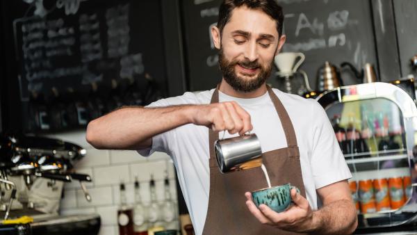 Man schenkt melk in kopje koffie in een café.