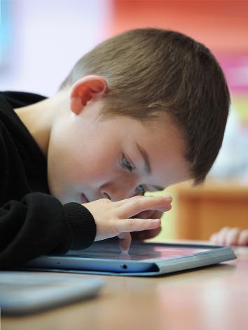 Kind hangt met zijn hoofd dicht boven een tablet die op tafel ligt