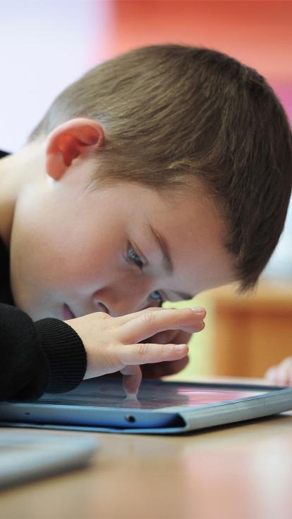 Kind hangt met zijn hoofd dicht boven een tablet die op tafel ligt