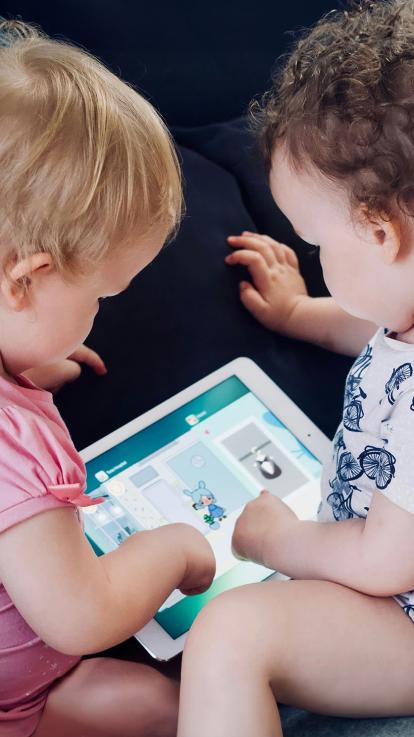 Twee baby's in rompers doen een spel op een tablet
