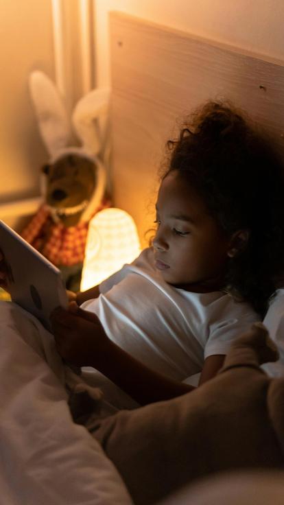 Kind kijkt naar een video op een tablet terwijl ze in bed ligt