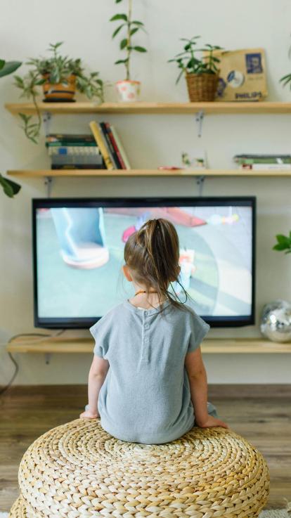 de rug van een kind dat zittend op een poef naar een televisie kijkt