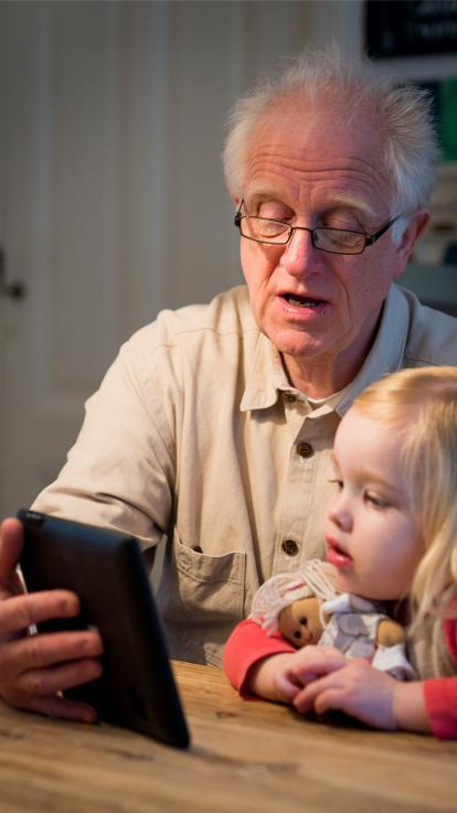 Opa kijkt op een tablet met een jong kind zittend aan tafel
