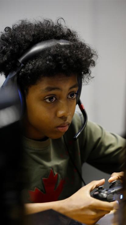 Een jongen kijkt naar computer met koptelefoon op en gamecontroller in hand