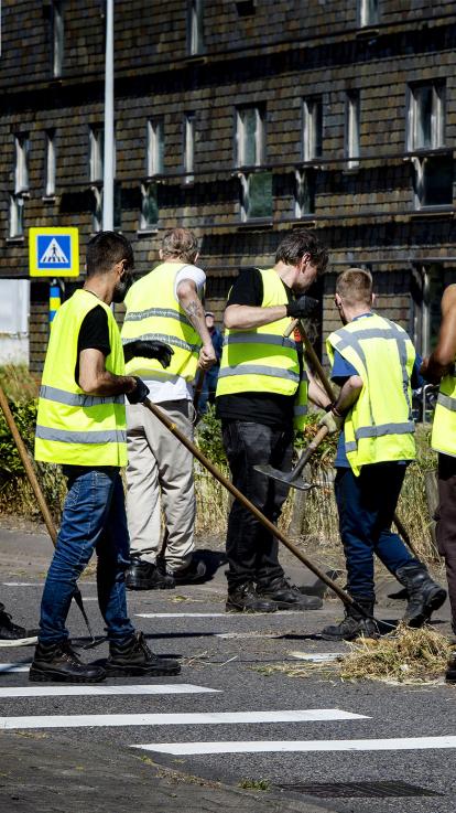 Een groep van vijf mannen ruimen in gele hesjes de straat op als taakstraf
