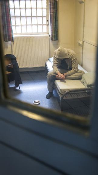 Door een gevangenisdeur zie je een man gebogen op bed zitten in een cel