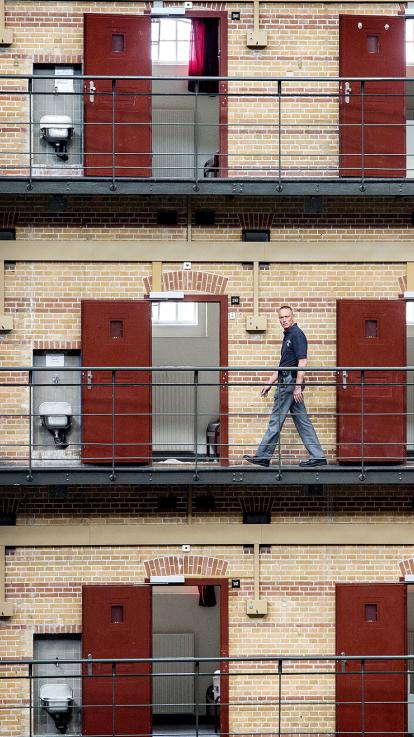 Een bewaker loopt langs lege cellen in een koepelgevangenis met meerdere verdiepingen
