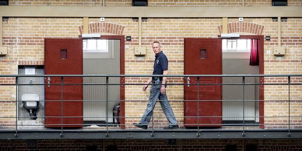 Een bewaker loopt langs lege cellen in een koepelgevangenis met meerdere verdiepingen