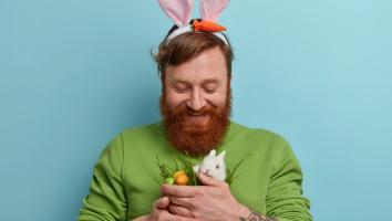 Man met baard heeft paasoren op en een konijntje en eitjes in zijn handen.