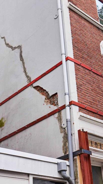 Huis met een grote scheur aan de zijkant wordt verstevigd met metalen platen.