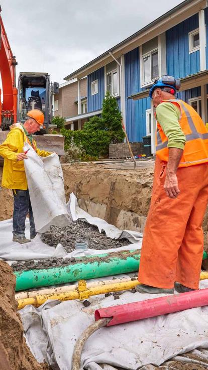In een woonwijk worden in de grond nieuwe buizen aangelegd en er wordt steen gestord.