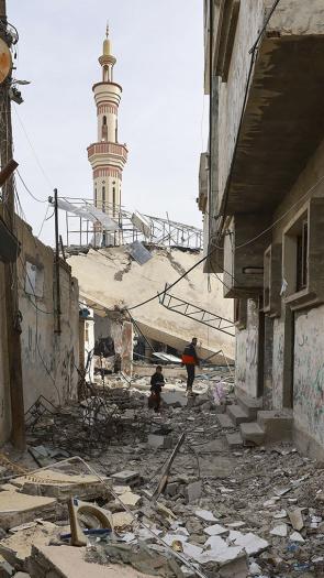 Man en jongen lopen door het puin van een moskee in Rafah