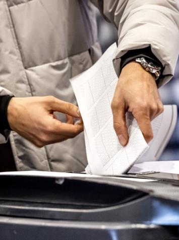 iemand stopt een stembiljet in de stemcontainer