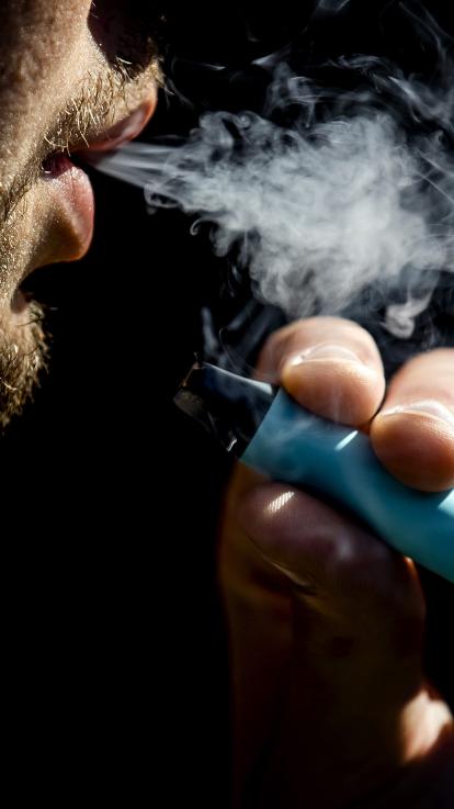 jongen blaast rook uit met blauwe wegwerpvape in zijn hand