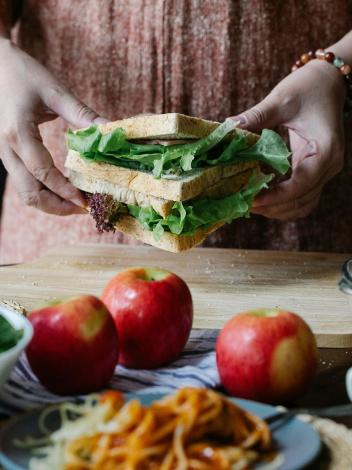 een tafel met producten waarachter je handen ziet die een sandwich vastpakken