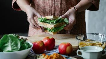 een tafel met producten waarachter je handen ziet die een sandwich vastpakken