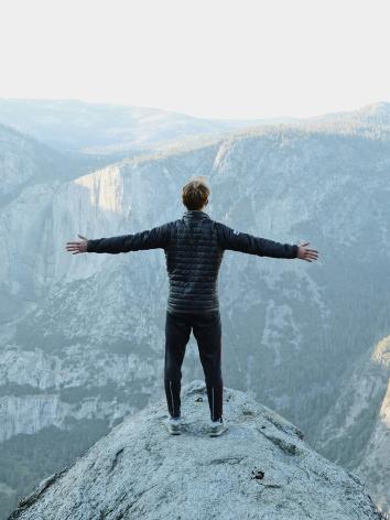 Jongen staat met armen wijd op bergtop