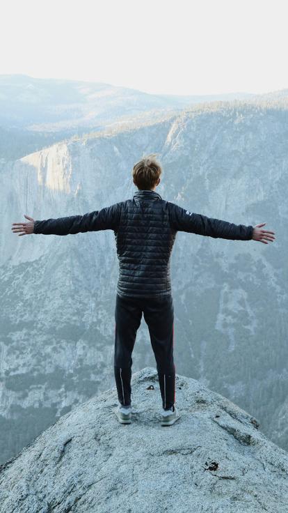 Jongen staat met armen wijd op bergtop