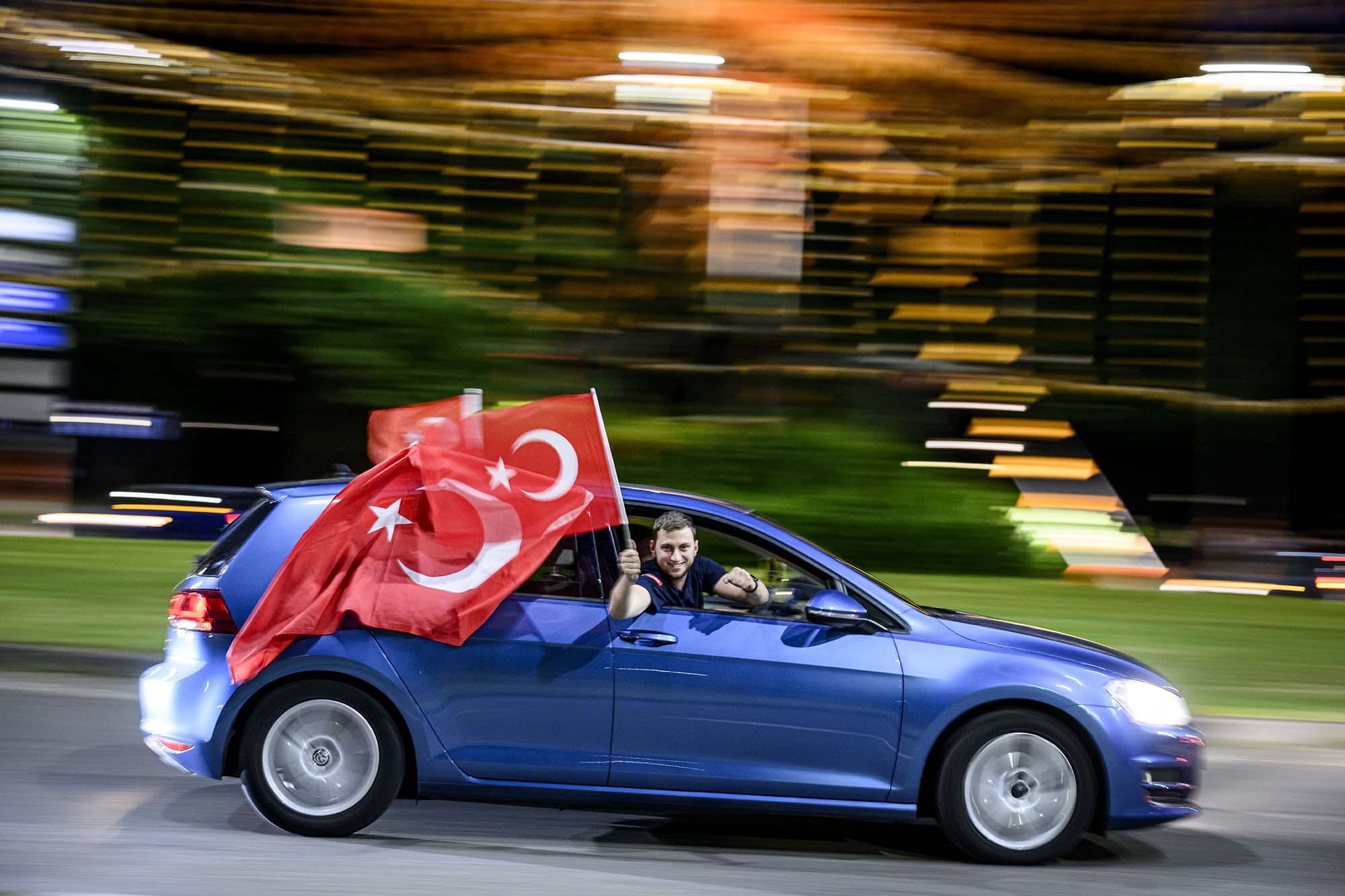 Man houdt Turkse vlag uit de auto terwijl de auto rijdt.