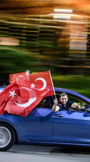 Man houdt Turkse vlag uit de auto terwijl de auto rijdt.