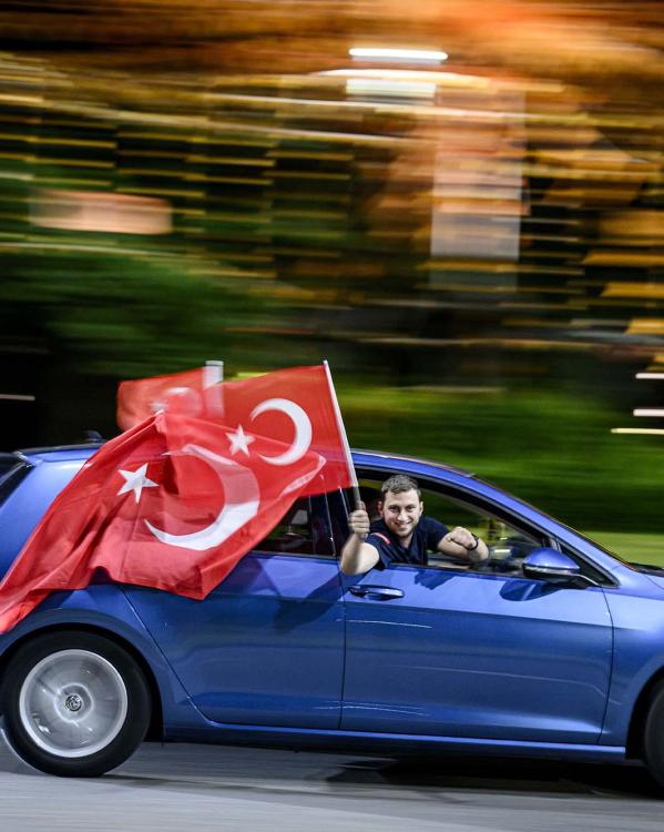 Man houdt Turkse vlag uit de auto terwijl de auto rijdt.