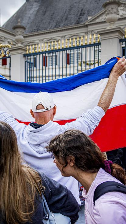 Man houdt omgekeerde Nederlandse vlag omhoog voor het paleis in Den Haag