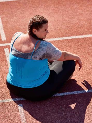 Vrouw zit bezweet op een atletiekbaan.