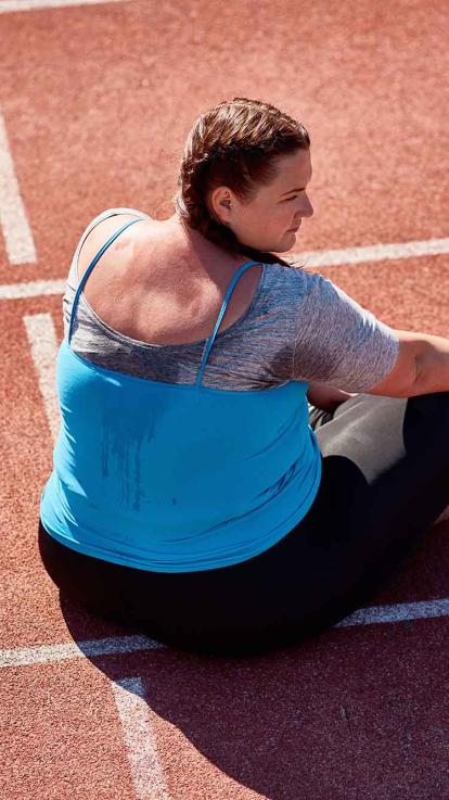 Vrouw zit bezweet op een atletiekbaan.