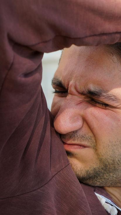 Man ruikt aan zijn oksel en kijkt vies.