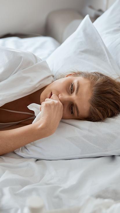 Vrouw ligt ziek in bed met een tissue in haar hand