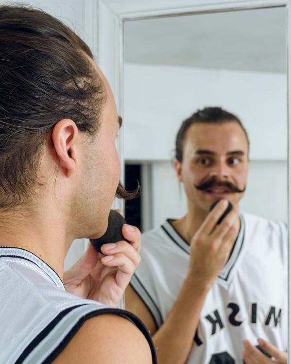 iemand met snor kijkt naar zichzelf in de spiegel en doet make-up op