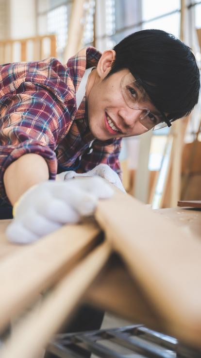 een houtbewerker kijkt naar de camera met planken in z'n handen