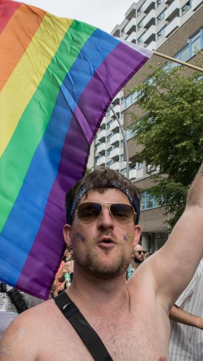 Meneer zonder shirt met zonnebril die met zijn hand de regenboogvlag ophoudt
