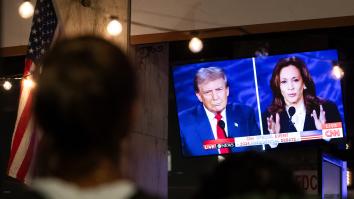 Een man kijkt naar het debat tussen Trump en Harris naast een Amerikaanse vlag