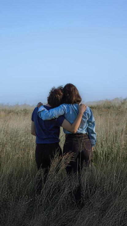 Twee vrienden staan met armen om elkaar heen in een veld. 