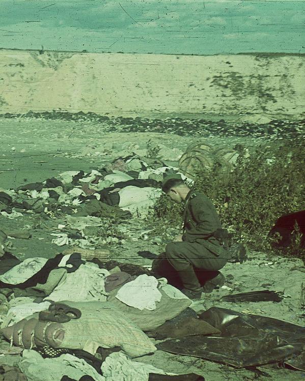 Soldaat zoekt door kleding van de slachtoffers van de Babyn Jar massa-executie tijdens de Holocaust