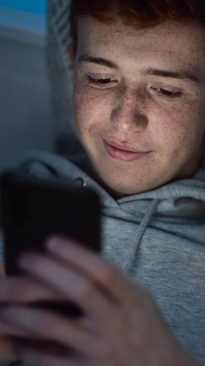 een tiener op z'n telefoon in het donker