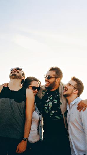 Vier vrienden staan lachend naast elkaar in de open buitenlucht.