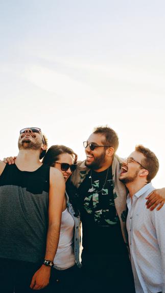 Vier vrienden staan lachend naast elkaar in de open buitenlucht. 