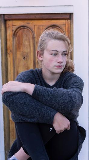 een tienermeisje staart buiten voor een huis voor zich uit