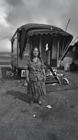  Een vrouw staat glimlachend voor haar woonwagen op een open terrein.