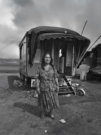 Een vrouw staat glimlachend voor haar woonwagen op een open terrein.