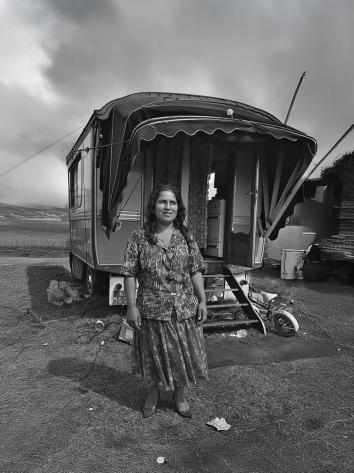  Een vrouw staat glimlachend voor haar woonwagen op een open terrein.