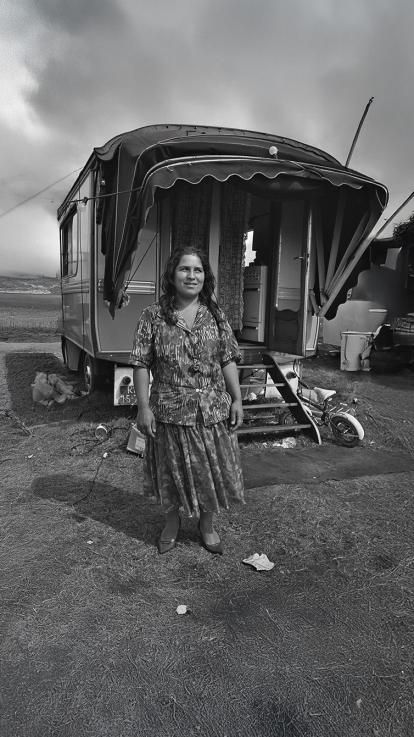  Een vrouw staat glimlachend voor haar woonwagen op een open terrein.