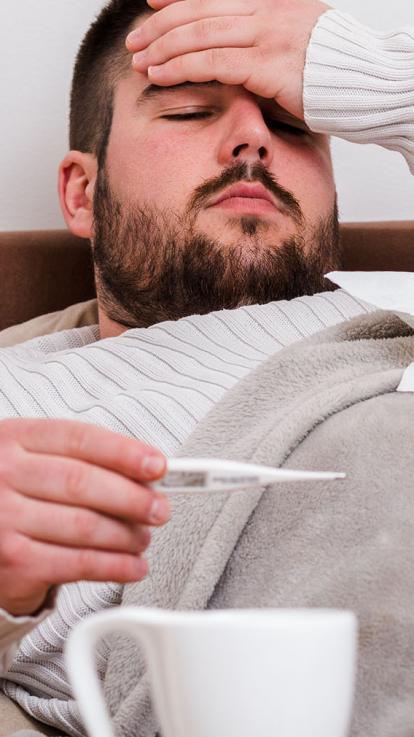 een zieke man in bed, met hand op voorhoofd en thermometer in andere hand