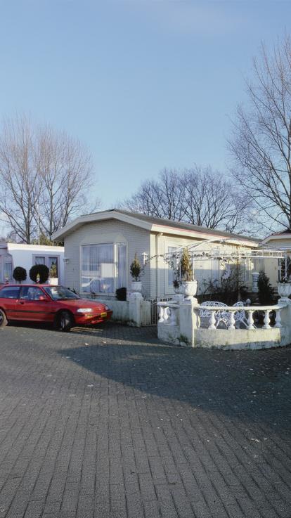 Een moderne woonwagen met een tuin en een rode auto.