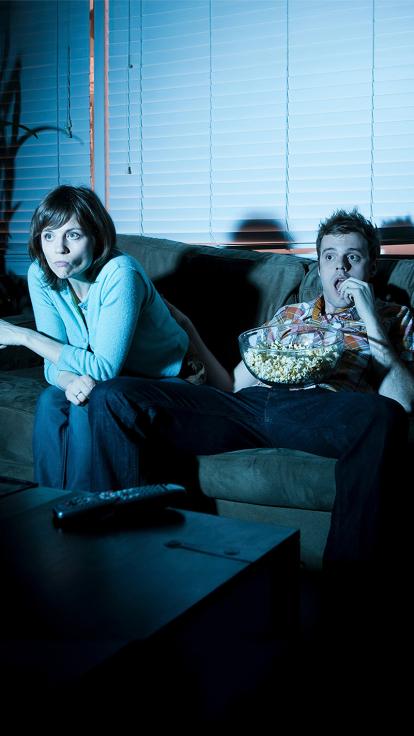 Twee mensen zitten op de bank tv te kijken met gespannen gezichten