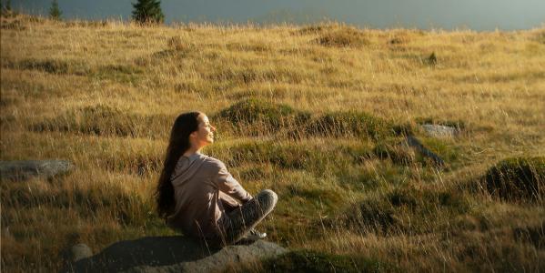 Meisje zit in grasveld in de zon en kijkt naar de lucht