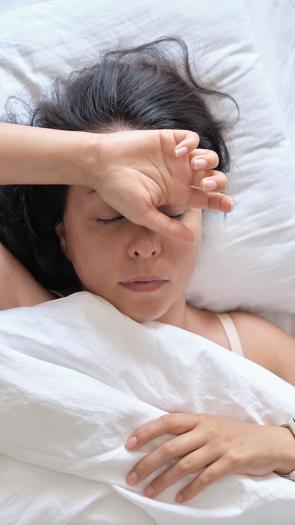 een vrouw in bed met de ogen dicht en een hand op haar voorhoofd