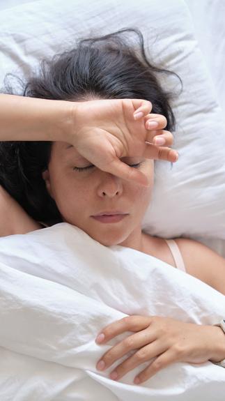 een vrouw in bed met de ogen dicht en een hand op haar voorhoofd